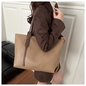 Détail de la texture en cuir tressé d'un grand sac cabas marron porté avec un look chic