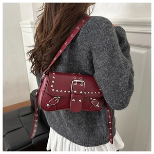Detail of burgundy leather shoulder bag with silver studs worn by a model in casual style