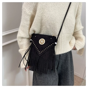 Detail of black suede crossbody bag with gold rivets, vintage stud, and long fringe