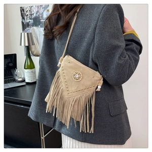 Detail of beige suede crossbody bag with metal rivets, fringe, and a rhinestone centerpiece