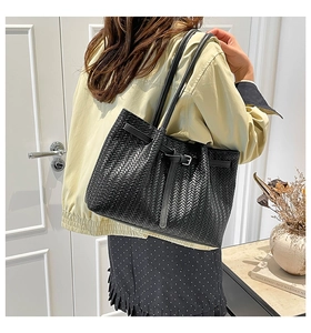 Detailed close-up of the black woven texture and leather strap on this stylish tote bag