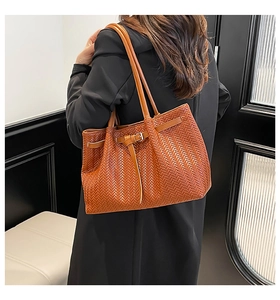 Detailed view of brown woven tote bag with V-shaped texture on black coat model