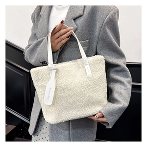 Detail of white plush bucket bag with leather handle and fashion tag on grey blazer