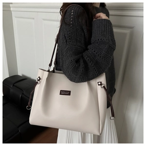 Detail of cream tote bag with adjustable brown strap and logo patch against a modern wall