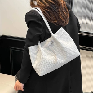 White woven tote bag with adjustable buckle strap held by model in black suit