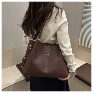 Detail view of large dark brown leather tote bag worn by model in a warm indoor setting
