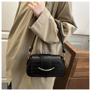 Détail du sac à main noir texture crocodile avec boucle dorée incurvée élégante sur le sac