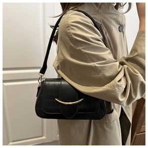 Détail du sac noir motif crocodile avec boucle dorée en croissant sur un trench-coat