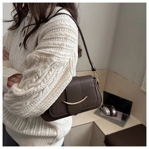 Sac bandoulière marron effet crocodile avec boucle dorée porté sur un pull blanc