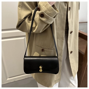 Detail of minimalist black leather crossbody bag featuring a gold buckle on khaki trench coat