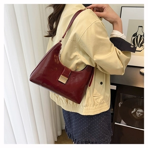 Detail view of burgundy patent leather crescent bag with golden buckle and sleek finish