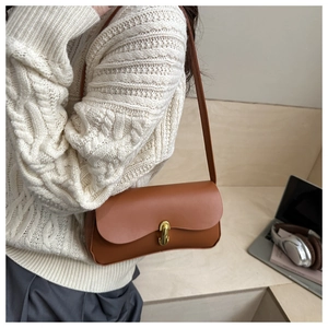 Close-up of brown leather shoulder bag with golden capsule clasp on white knit sweater