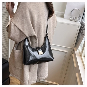 Detail of black glossy patent leather shoulder bag with metallic buckle on a model