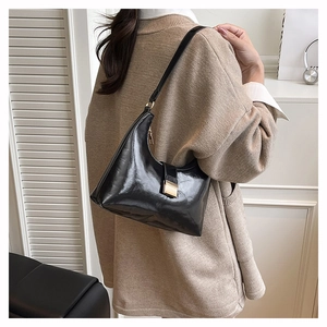 Detail of a black hobo bag with a golden metal buckle worn on the shoulder
