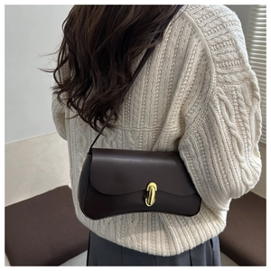 Detail shot of a dark brown leather underarm bag with a golden metal clasp on a beige sweater