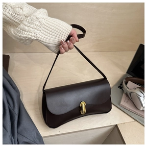 Detail of dark brown leather handbag with gold capsule lock on a minimalist wood surface