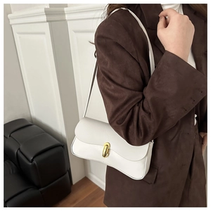 Detailed close-up of white leather underarm bag featuring a minimalist oval gold metal clasp