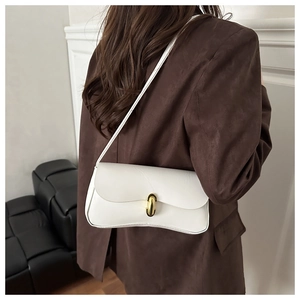 Detail of cream half-moon underarm bag with gold metal clasp on a dark blazer