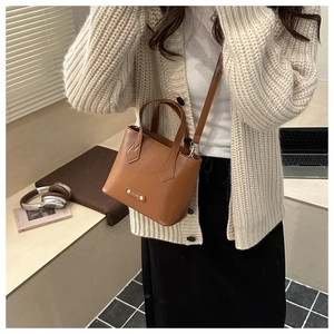 Borsa a secchiello marrone abbinata a un maglione bianco e gonna nera per un look casual