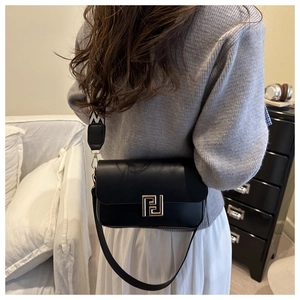 Close-up of black crossbody bag with gold hardware and geometric woven strap detail