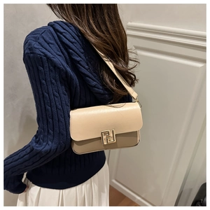 Detail of a beige and tan leather shoulder bag with a gold geometric clasp on a model