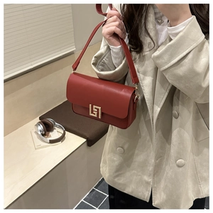 Detail of burgundy leather handbag with gold geometric lock and wide shoulder strap