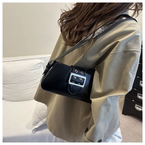 Side view of a glossy black underarm bag with a large silver buckle on a model