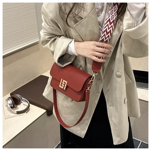 Detail of red crossbody bag with broad woven strap and large golden square buckle