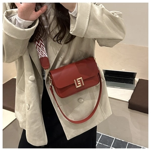 Close-up of deep red leather crossbody bag with golden geometric lock and patterned strap