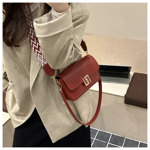 Detail of red leather crossbody bag with golden geometric buckle and patterned strap
