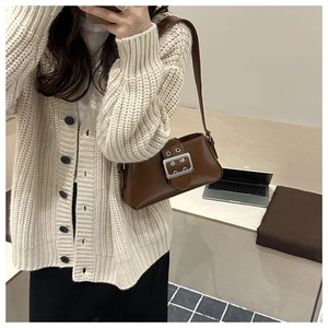 Detailed view of brown leather underarm bag with silver buckle worn with a knit cardigan