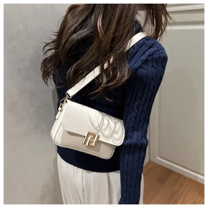 Close-up of cream leather baguette bag with gold metal clasp and wide shoulder strap