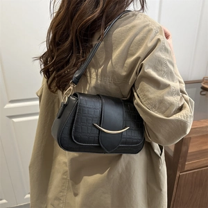 Sac bandoulière noir motif crocodile avec boucle dorée en croissant porté par un mannequin