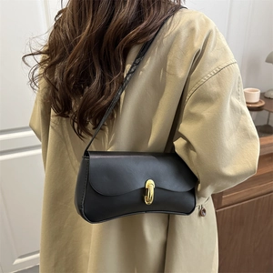 Minimalist black leather baguette bag with gold lock shown on shoulder for daily style