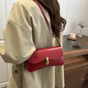 Minimalist red leather underarm bag with gold lock worn over a stylish beige coat