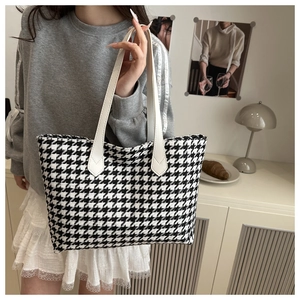 Detail of black and white houndstooth travel tote with white leather handles in home setting