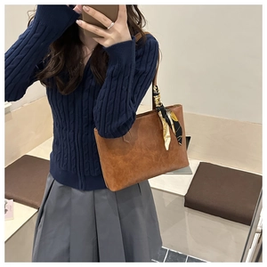 Brown leather tote bag detail with decorative floral scarf handle and neat stitching