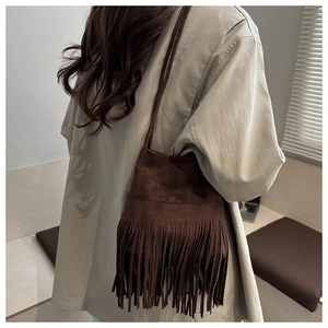 Détail du sac seau en daim marron foncé avec de longues franges bohèmes et fines lanières
