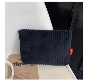 Detailed view of black corduroy clutch bag texture with a red fashion woven label