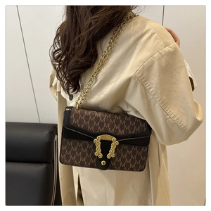 Detailed shot of retro shoulder bag with M-pattern texture and gold chain on model