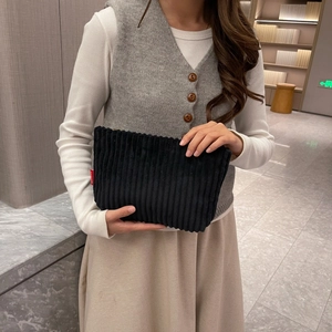 Detail of black corduroy envelope clutch with red Fashion label held by model