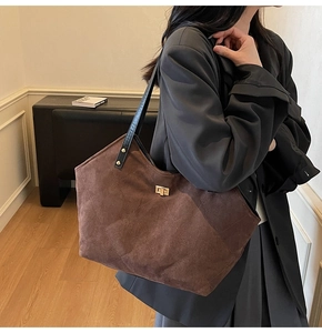 Detail view of large brown quilted suede tote bag with golden lock on model shoulder
