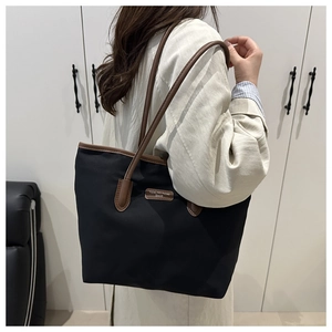 Detail of a large capacity tote bag with black fabric and brown leather trim on model