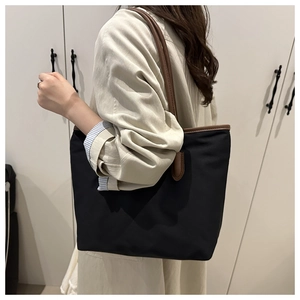Detail of black nylon tote bag with brown leather straps shown on model for daily commute