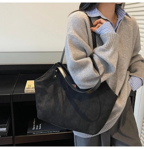 Detail of a black large tote bag with matte texture and silver rivets on a model's shoulder