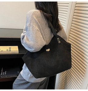 Detail of black faux suede tote bag featuring a gold twist lock and sturdy shoulder straps