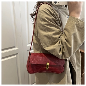 Détail du sac bandoulière en cuir bordeaux à motif crocodile avec fermoir doré sur manteau