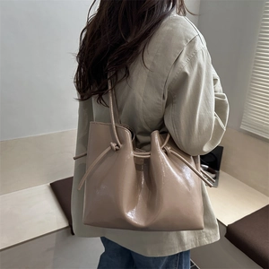 Beige patent leather tote bag with side knot details shown on a model in a minimalist room