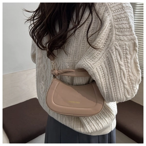 Detail of beige half-moon shoulder bag with knot strap on a cream knit sweater