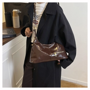 Brown glossy patent leather hobo bag with gold zipper detail worn by a model in a cafe